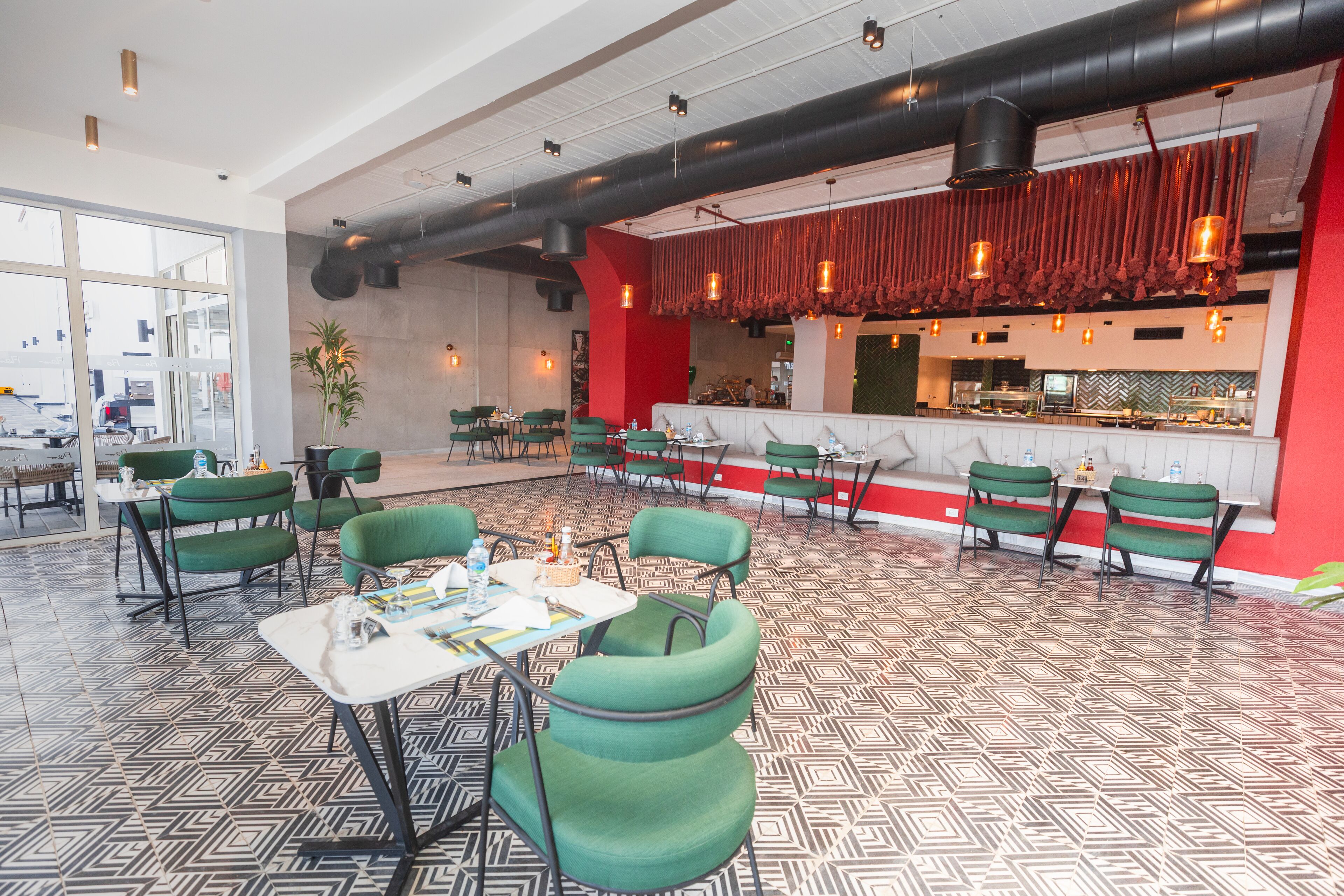 A restaurant with green chairs, a patterned floor, and a red accent wall.