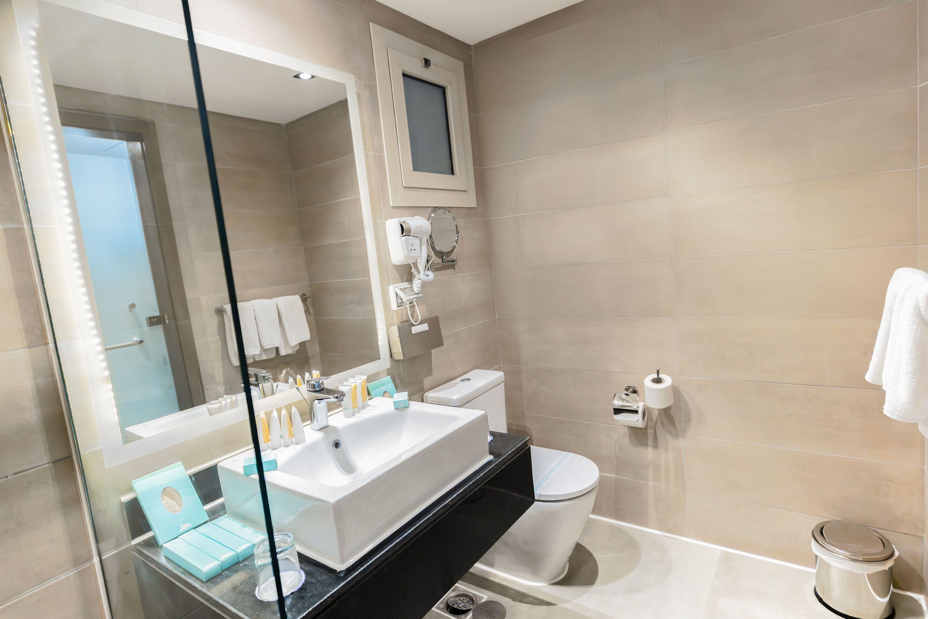A modern bathroom with a large mirror, a white sink, a toilet, and a glass shower enclosure.