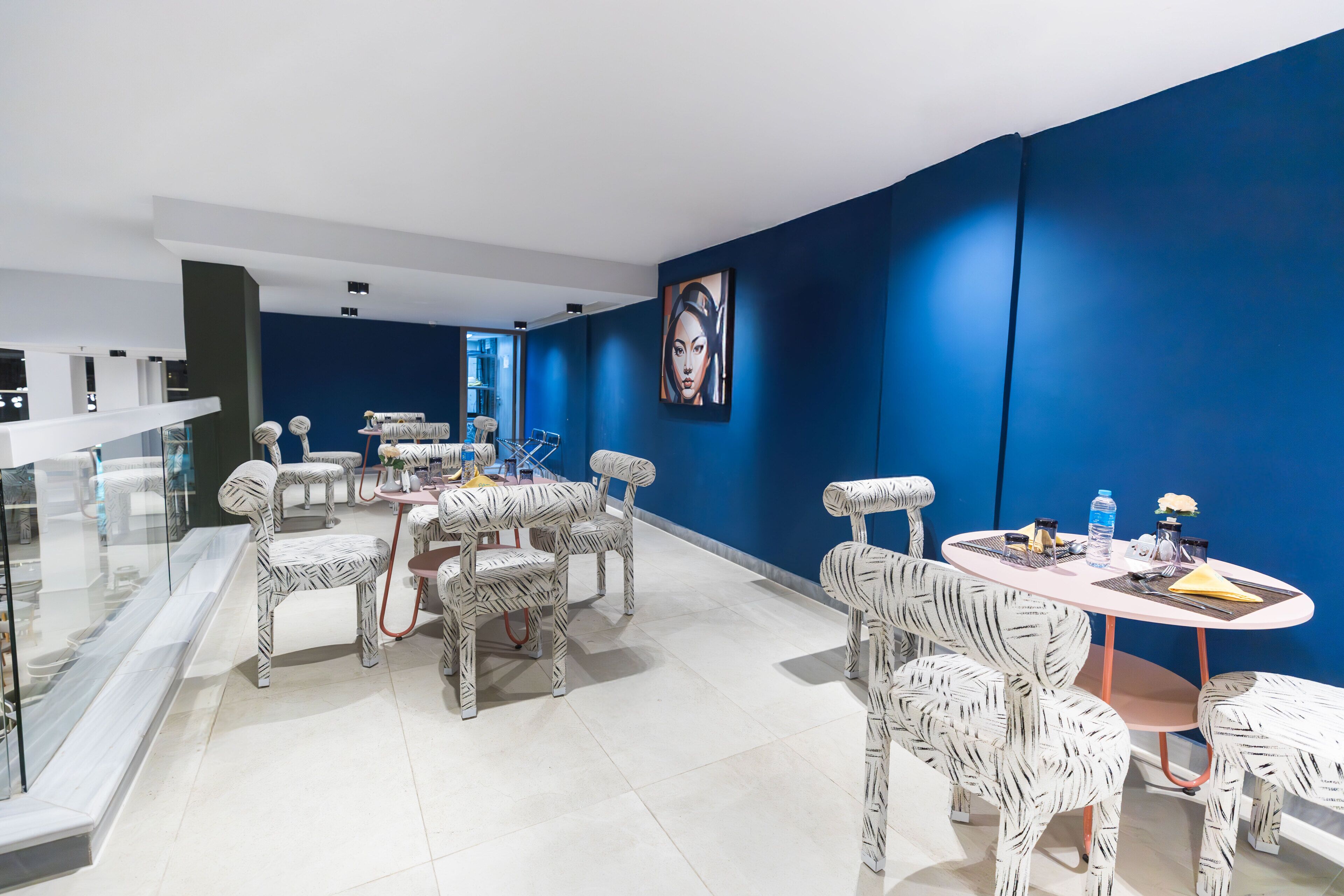 A modern dining area with zebra-patterned chairs and a round table, set against a blue wall with a large painting.