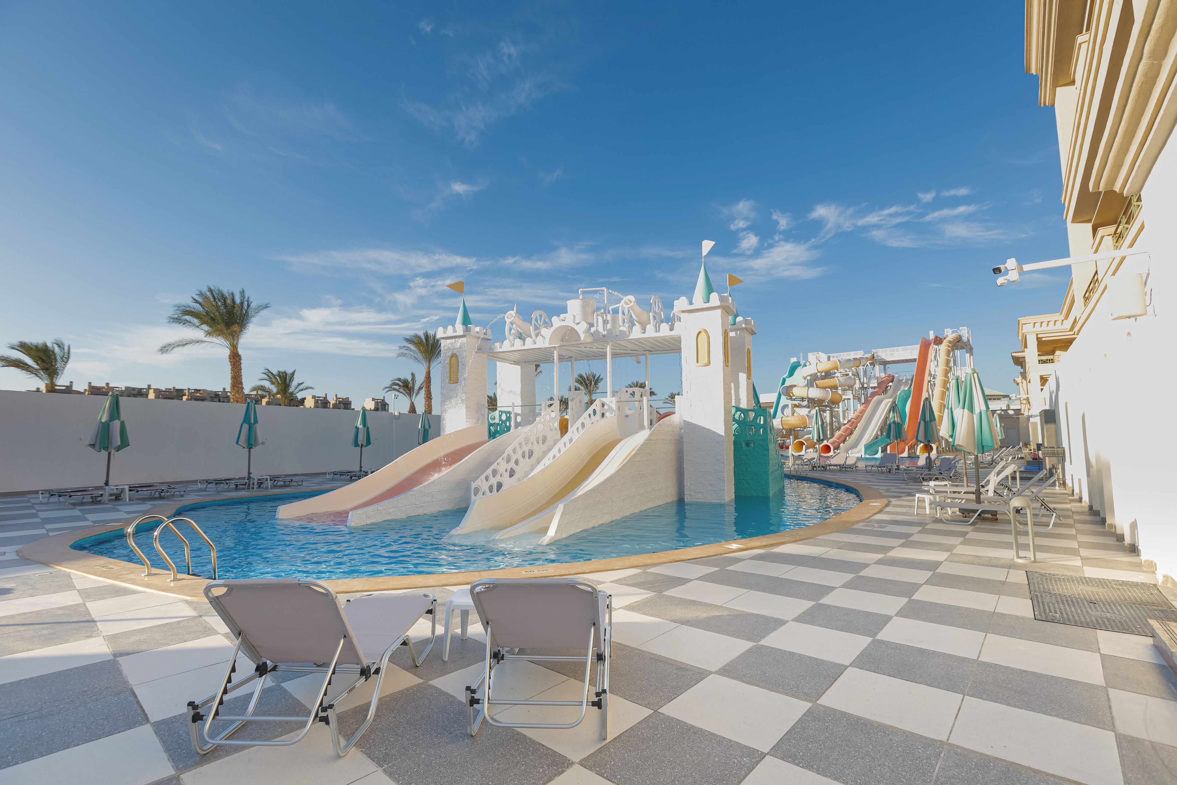 Un espace piscine doté d’un toboggan aquatique sur le thème d’un château, de chaises longues et de parasols.
