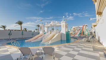 Un espace piscine doté d’un toboggan aquatique sur le thème d’un château, de chaises longues et de parasols.