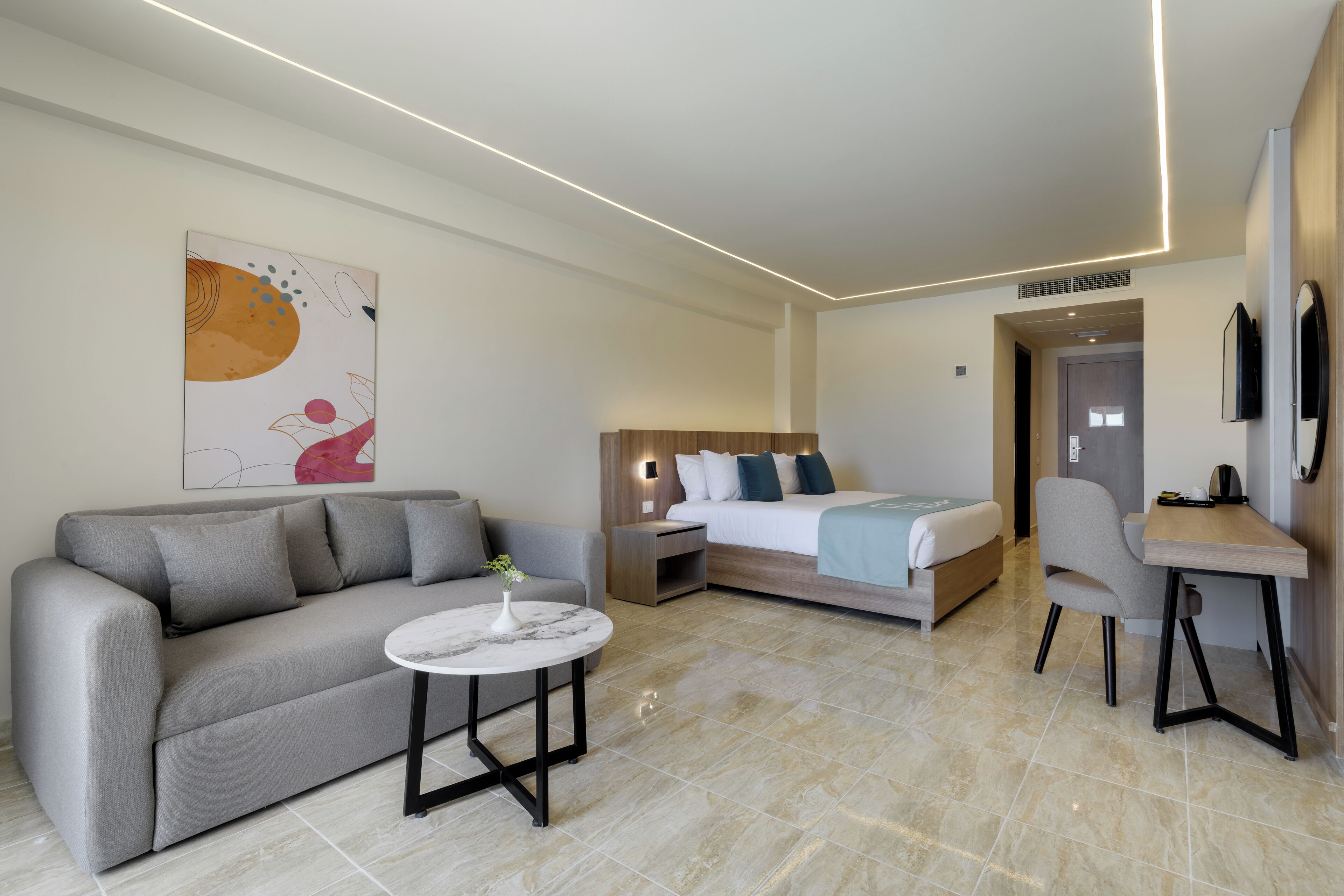 A modern hotel room with a sofa, a bed, a desk, and a small table.