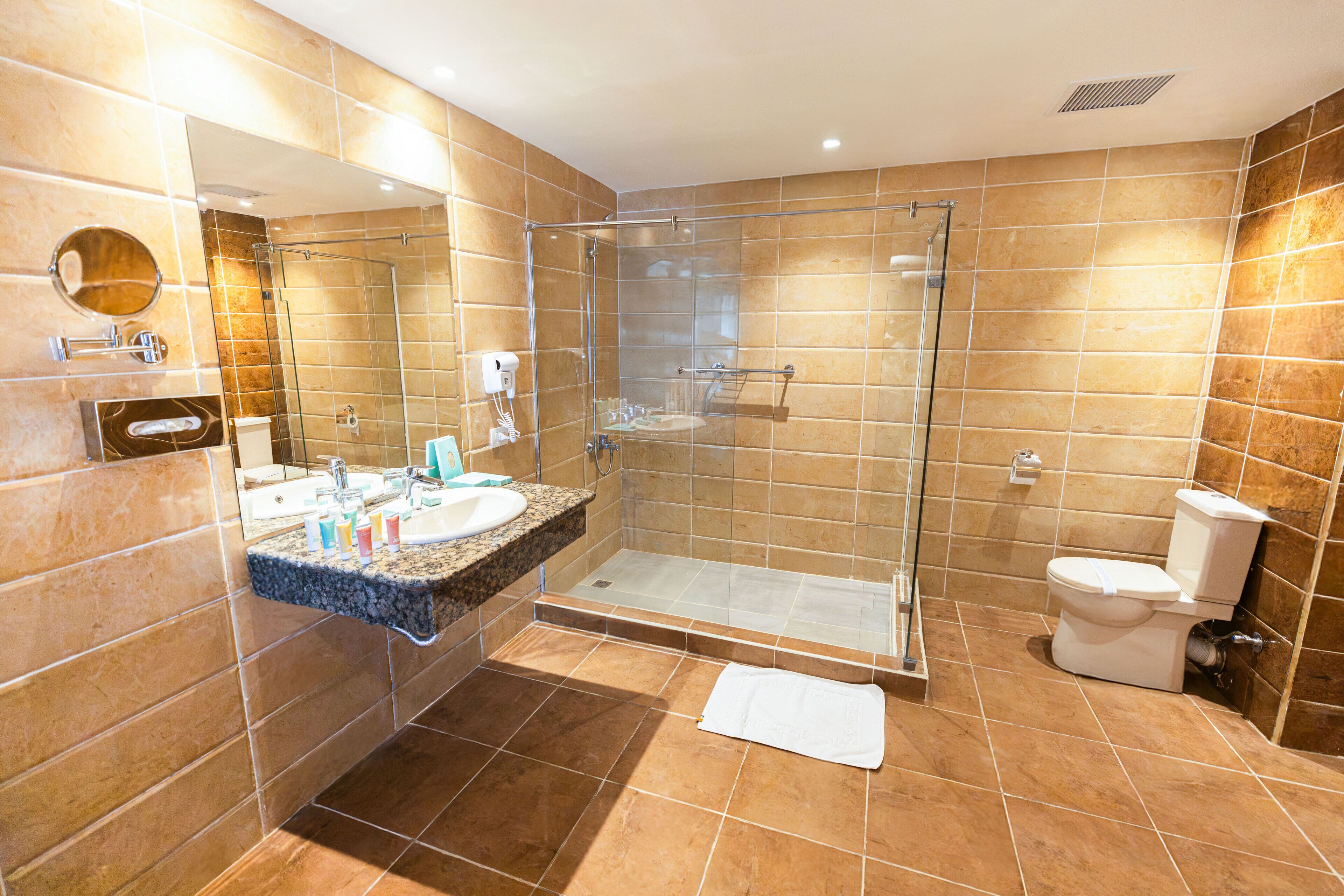 Un baño moderno con ducha de vidrio, lavamanos con encimera de mármol y un inodoro.