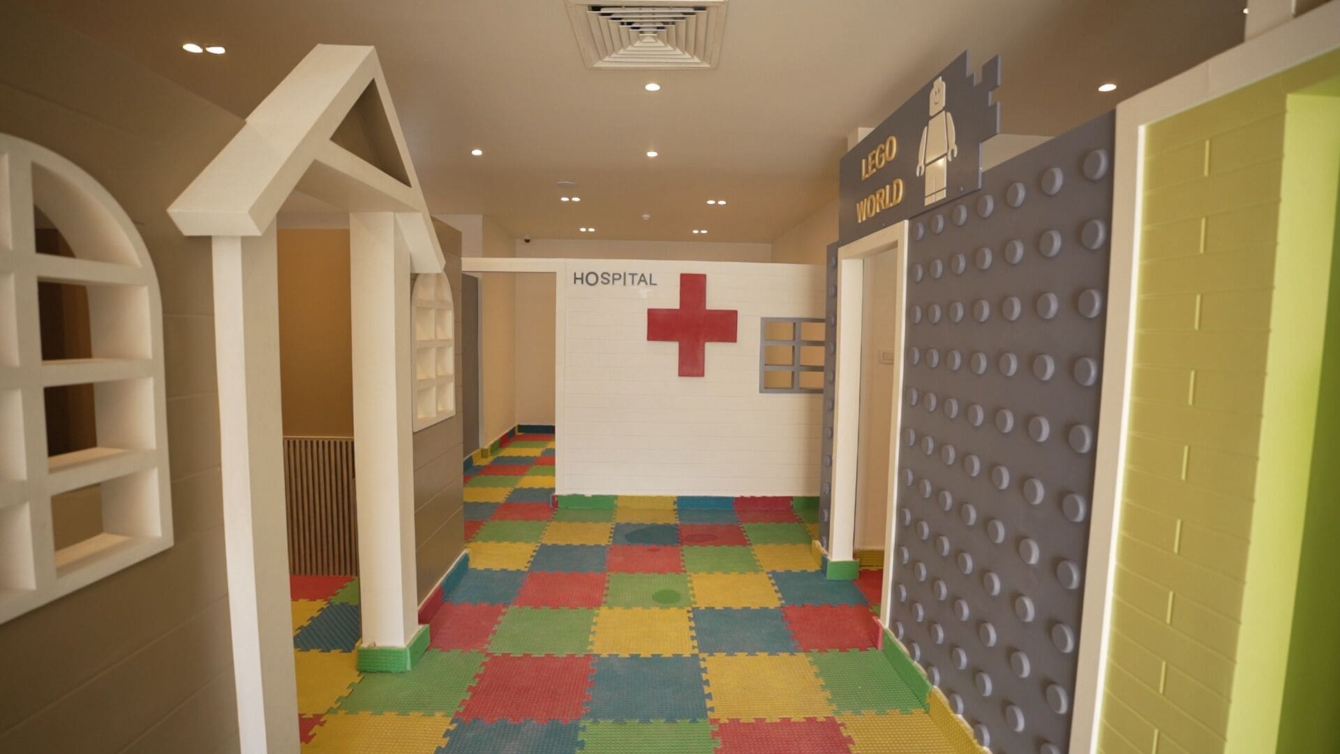 A children's play area with a hospital-themed wall, colorful interlocking foam tiles on the floor, and a LEGO wall.