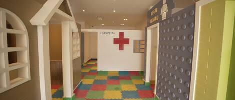A children's play area with a hospital-themed wall, colorful interlocking foam tiles on the floor, and a LEGO wall.
