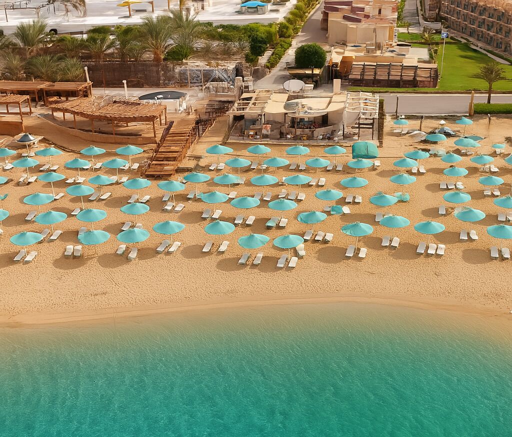 An aerial view of a beach with numerous turquoise umbrellas and white lounge chairs.