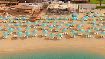 An aerial view of a beach with numerous turquoise umbrellas and white lounge chairs.