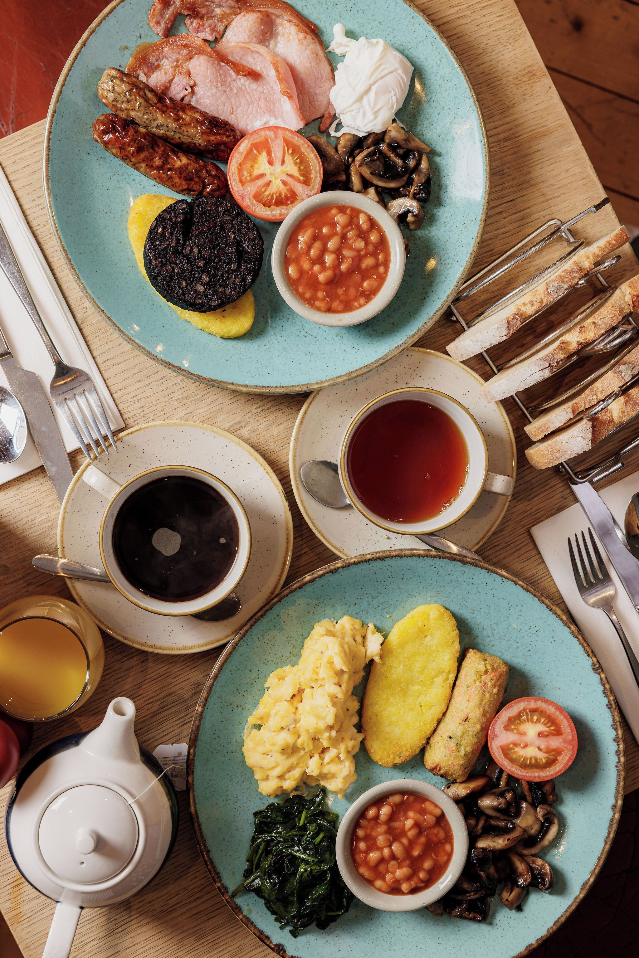 A breakfast table with plates of food, cups of beverages, and cutlery.