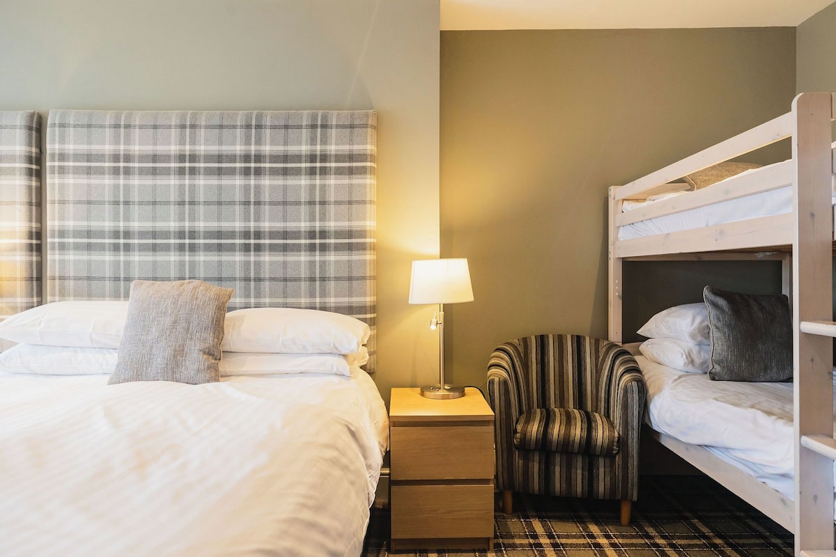 Una habitación de hotel con una cama, una mesita de noche con una lámpara, una silla a rayas y una cama nido.
