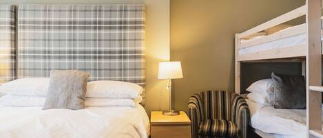 A hotel room with a bed, a nightstand with a lamp, a striped chair, and a bunk bed.