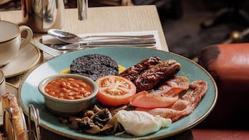 Un plato de desayuno con frijoles, tomates, champiñones, tocino y huevos sobre una mesa con una tetera y una taza.