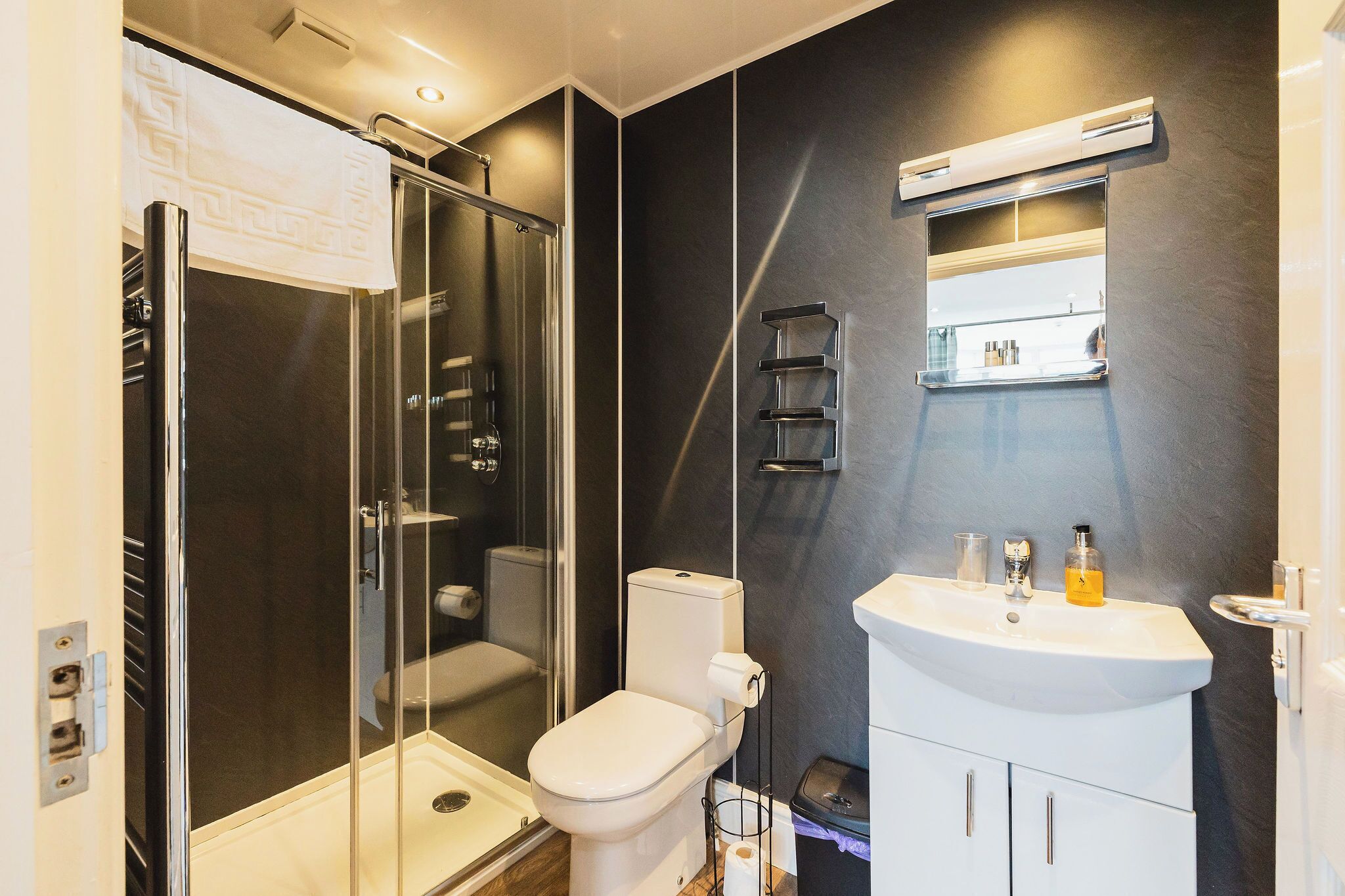 Un bany modern amb dutxa d'estuc de vidre, un vàter blanc i un lavabo blanc amb un mirall a sobre.