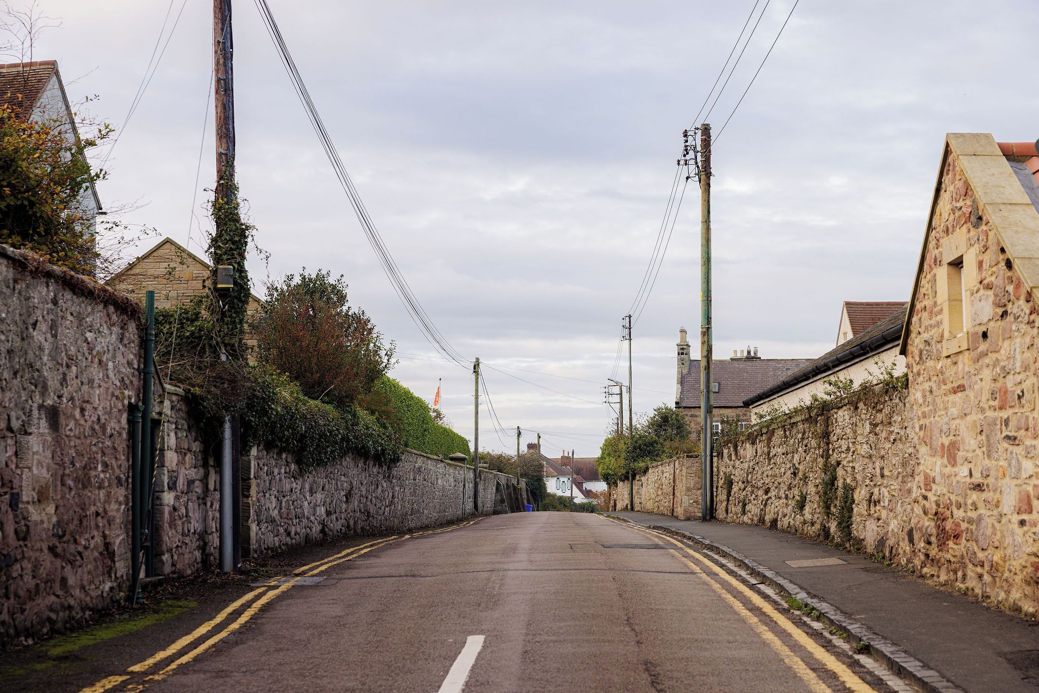 A narrow street flanked by stone walls and utility poles.