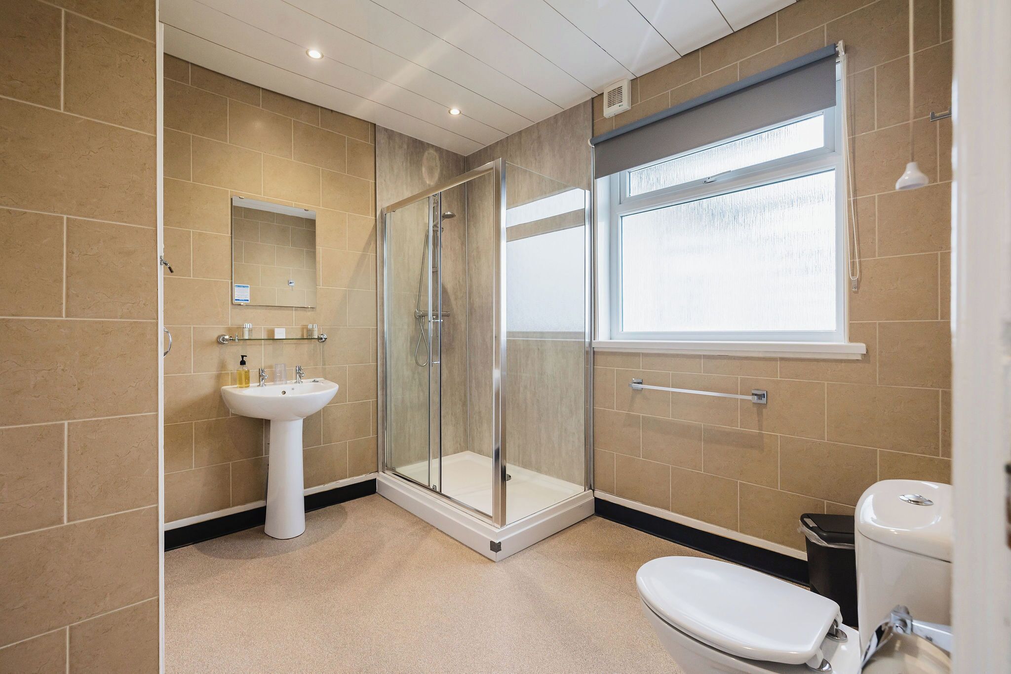 Un baño moderno con ducha de vidrio, lavabo pedestal y retrete.