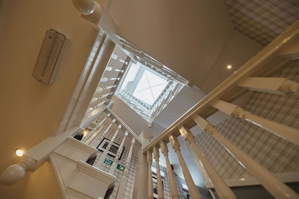 Une vue d’un escalier avec un plafond en verre, des rampes blanches et un panneau de signalisation verte indiquant la sortie.