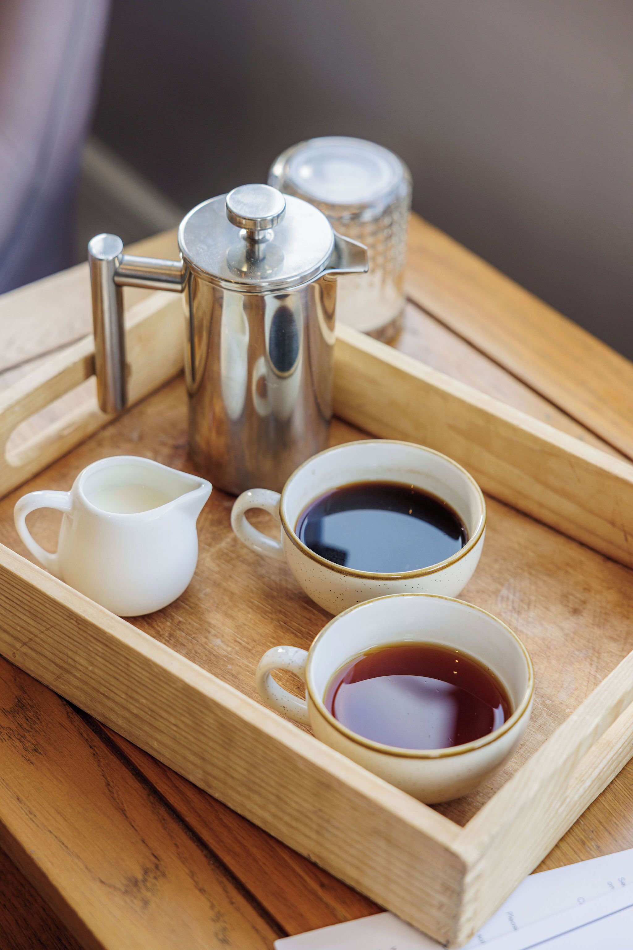 A tray with a coffee pot, a milk jug, and two cups of coffee on a wooden table.