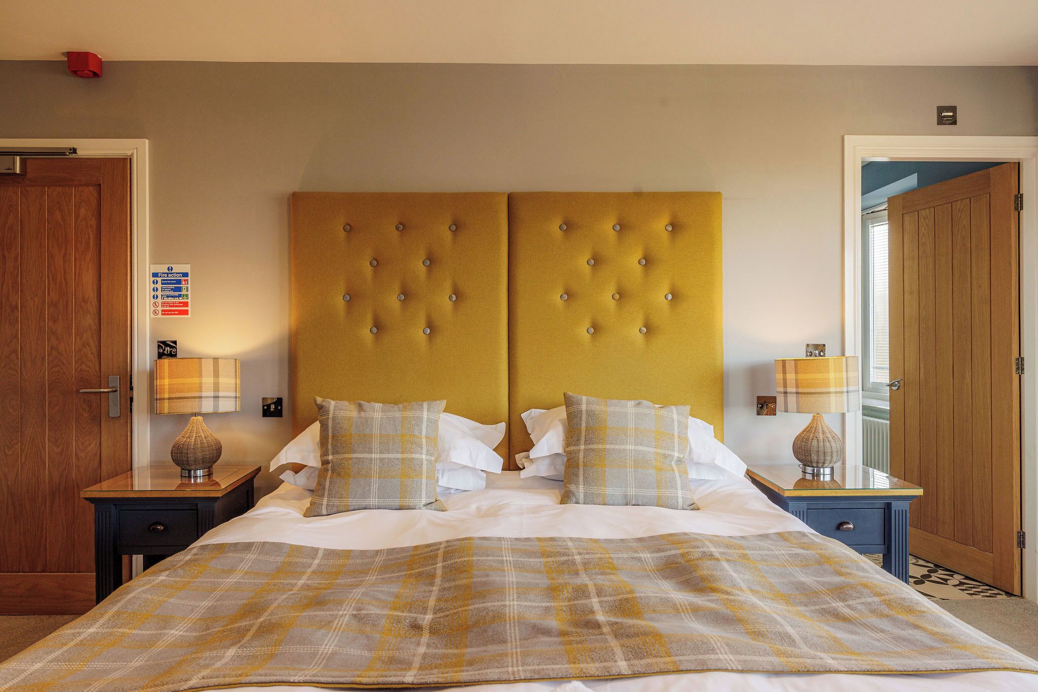 Une chambre d’hôtel avec un grand lit, deux tables de chevet, une porte en bois et un détecteur d’incendie bien visible.