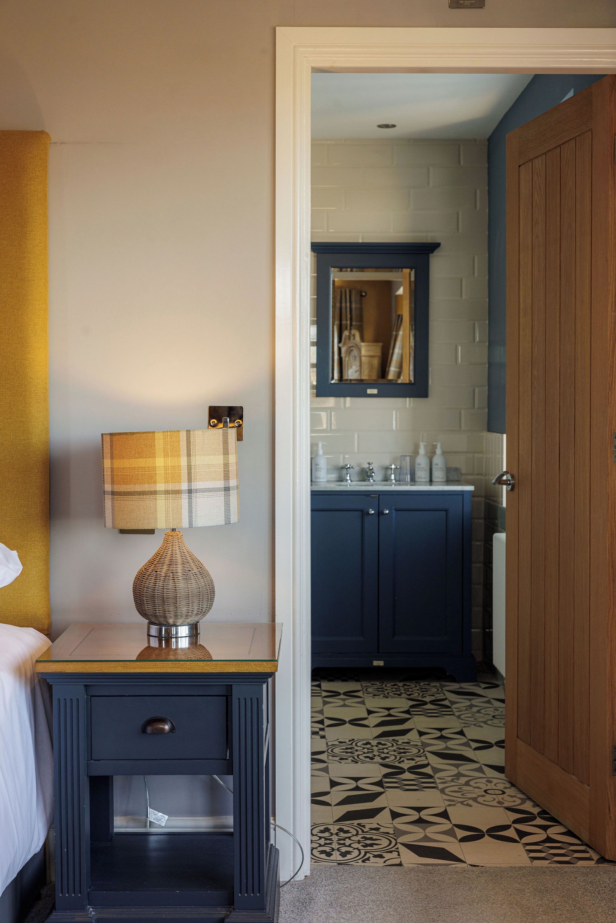 A bedroom with a bed, a bedside table with a lamp, a dresser, and a mirror.