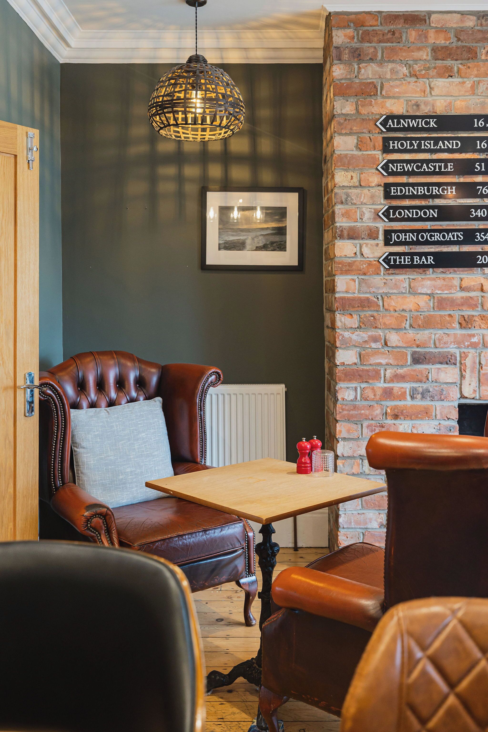 A cozy room with a leather armchair, a wooden table, and a brick wall with a directional sign.