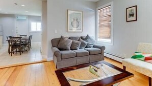 Ein Wohnzimmer mit grauem Sofa, einem Couchtisch und einem Essbereich mit Stühlen und Tisch.