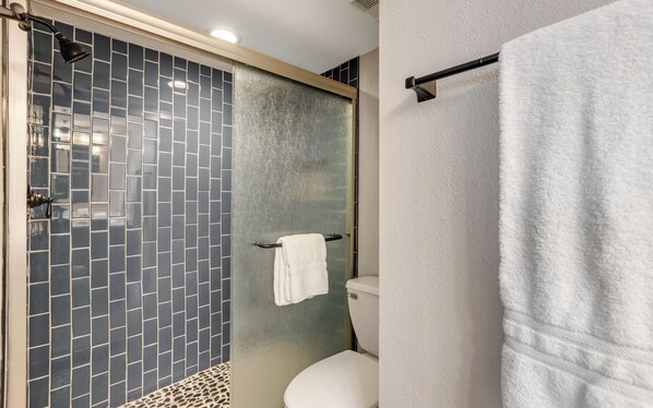 Une salle de bain avec une douche à parois de verre, des toilettes blanches et un porte-serviettes.