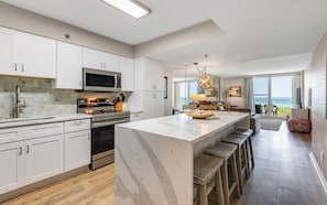 A modern kitchen with white cabinetry, a central island with stools, a microwave, stove, and oven. - Beachfront Condo + Community Pool, & Stunning View (Santa Rosa Beach)