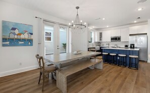 Una cocina moderna con armarios blancos, una isla central con taburetes, una lámpara de araña y un cuadro en la pared.