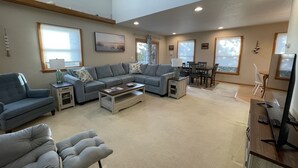 A spacious living room with a sectional sofa, a dining table, and a flat-screen TV. - Island Dreaming Retreat 3 Bedroom Cottage (Frisco)