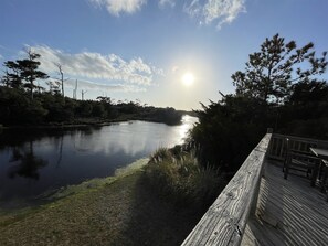 Una terraza de madera con vistas a un río tranquilo, árboles y cielo despejado.