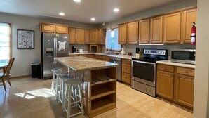 A modern kitchen with wooden cabinets, stainless steel appliances, and a central island with stools. - Island Dreaming Retreat 3 Bedroom Cottage (Frisco)