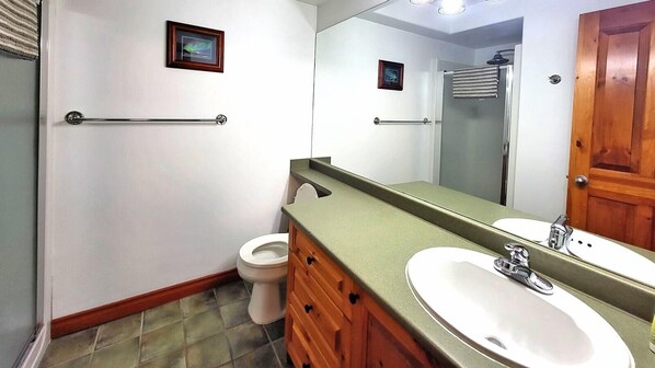 A bathroom with a toilet, a sink, a mirror, and wooden cabinets. - Timberline Village #12 Home (Sun Peaks)