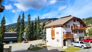 Un immeuble de deux étages doté d’un balcon, d’un garage et d’un espace de stationnement où sont garées des voitures.