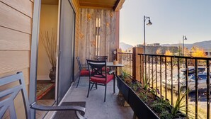 A balcony with a wooden ceiling, a table with chairs, a potted plant, and a view of a parking area with cars and mountains in the background. - Sail Lofts 101 2 Bedroom Condo (Dillon)