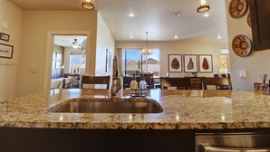 A kitchen with granite countertops, stainless steel sink, pendant lighting, and a view to the dining area. - Sail Lofts 101 2 Bedroom Condo (Dillon)