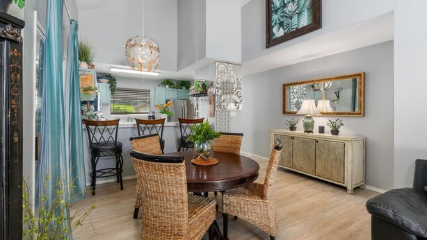 A dining area with a round table, wicker chairs, a cabinet with potted plants, and a large mirror on the wall.