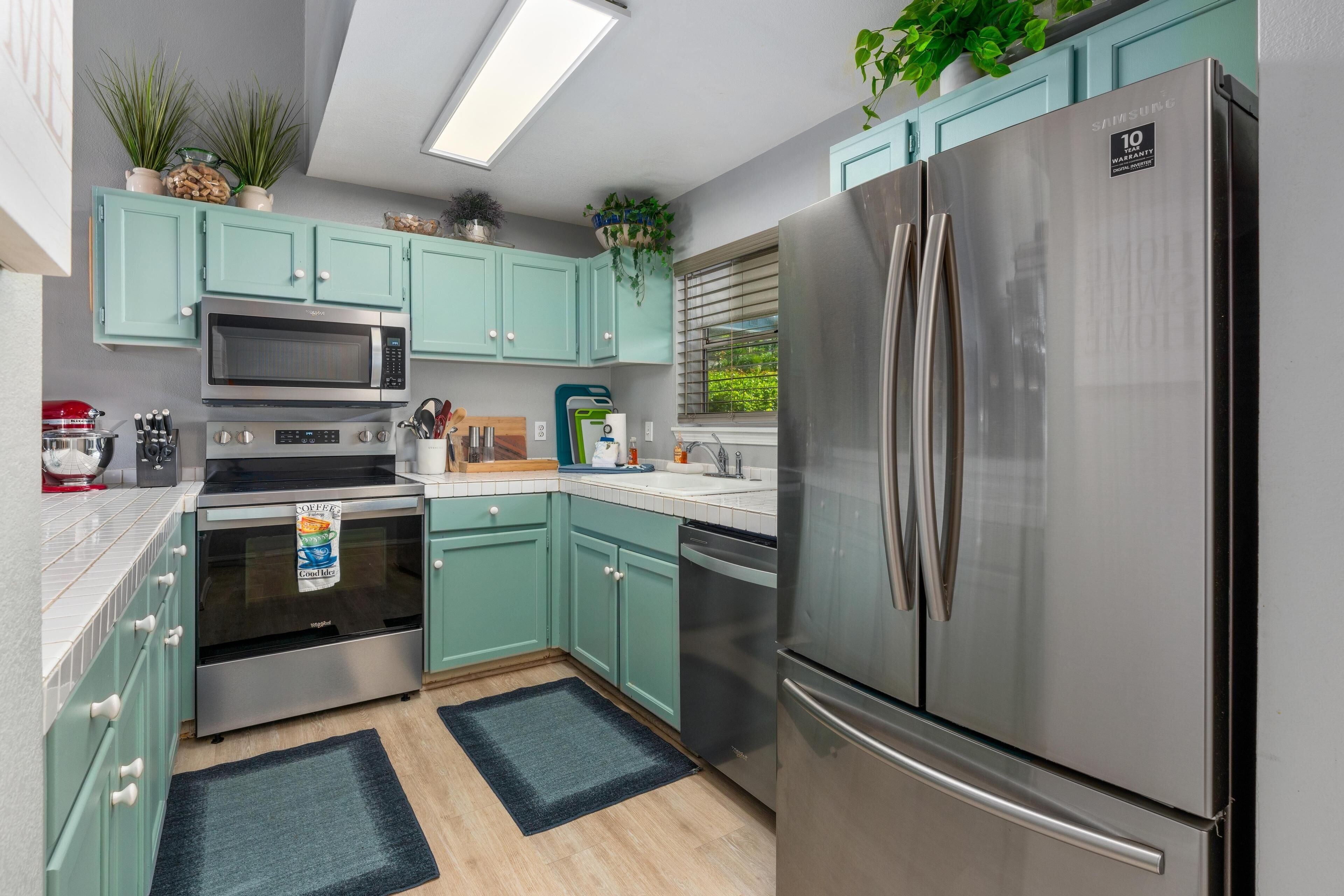 Une cuisine moderne avec des armoires de couleur turquoise, des appareils électroménagers en acier inoxydable et un grand réfrigérateur.