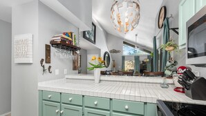 A kitchen with green cabinets, a white tiled backsplash, and a hanging light fixture.