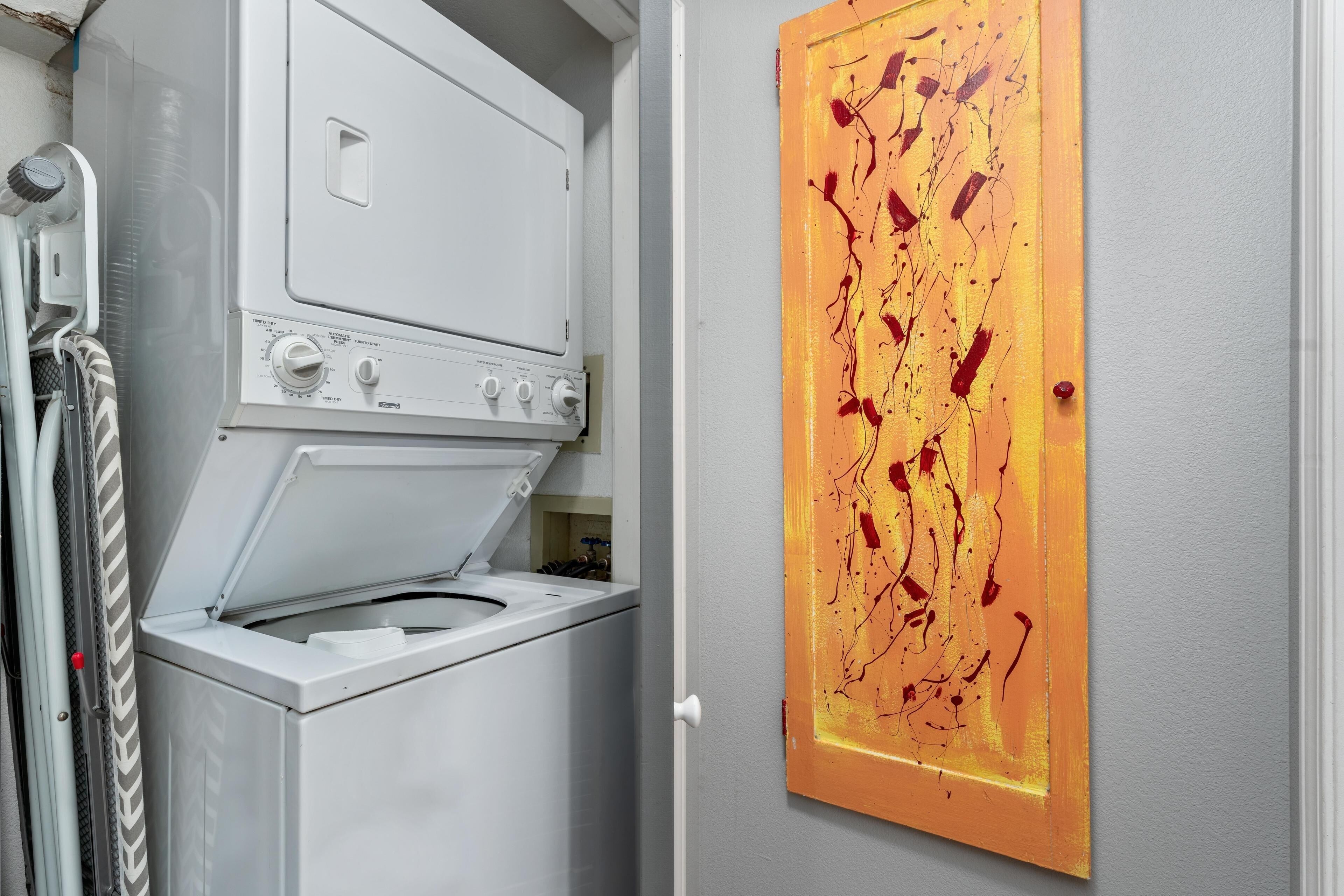 A laundry area with a washing machine and dryer, a towel rack, and a painting on the wall.