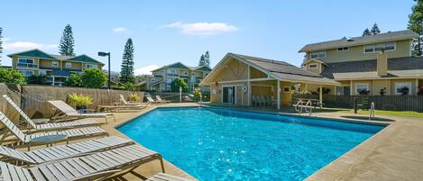 A rectangular swimming pool with lounge chairs and a covered area, surrounded by residential buildings.
