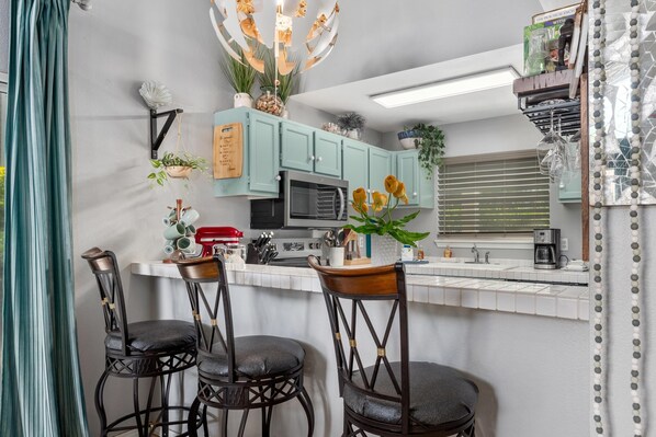 A modern kitchen with teal cabinets, a central island with bar stools, and various kitchen appliances.