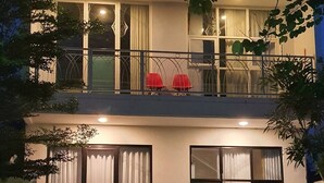 Ein zweistöckiges Gebäude mit Balkon, großen Fenstern und einer kleinen Sitzgelegenheit im Freien mit roten Stühlen.