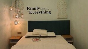 Ein Schlafzimmer mit einem Bett, einer Wand mit einem Zitat zum Thema Familie und hängenden Pendelleuchten.