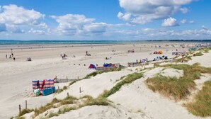 Ein breiter Sandstrand mit Zelten und einem Zaun.