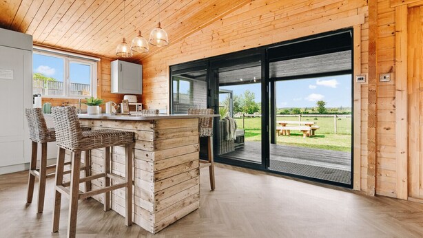 Ein Holzinnenraum mit Küchenzeile, Barhocker und Blick durch eine Glastür auf eine Terrasse.