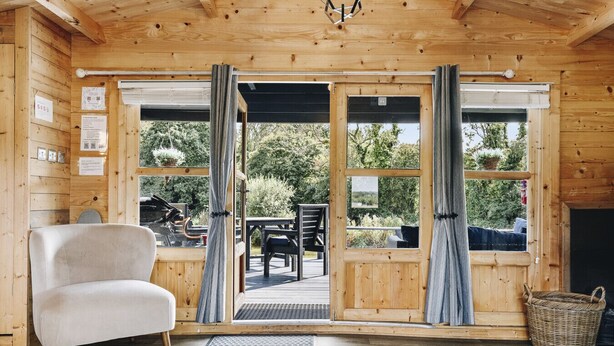 A cozy room with a large wooden door leading to an outdoor deck, a comfortable chair, and a wicker basket.