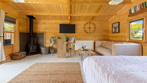 A cozy log cabin interior with a fireplace, a sofa, a dining table, and a bed.