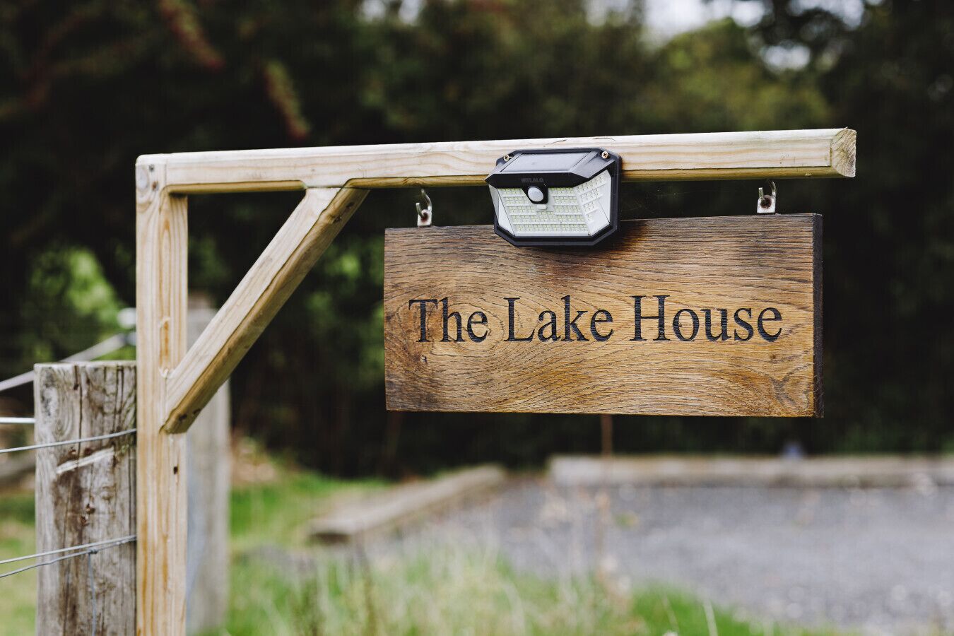 Ein hölzernes Schild mit der Aufschrift 'The Lake House', befestigt an einem Holzpfosten.