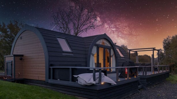 Een gezellig vakantiehuis met een groot dakvenster, een terras met buitenmeubels en uitzicht op de nachthemel.
