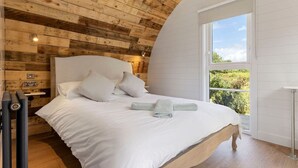 Een slaapkamer met een houten plafond, een groot raam en een bed met witte lakens.