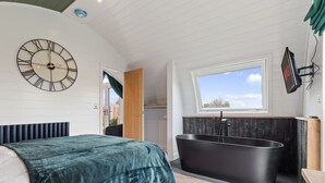 A modern bedroom with a large bed, a black bathtub, a large wall clock, and a window with a view.